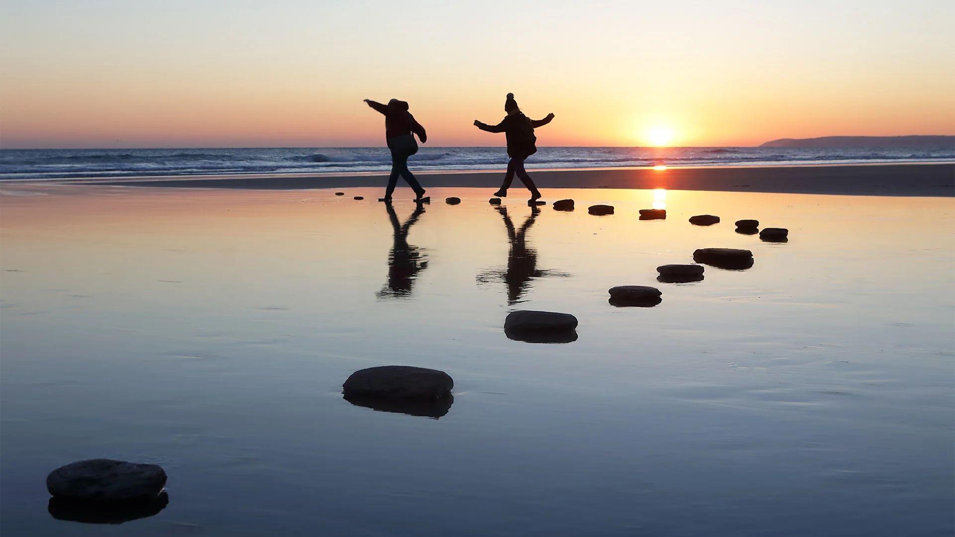 Personas camiando sobre rocas en sobre el agua al atardecer.
