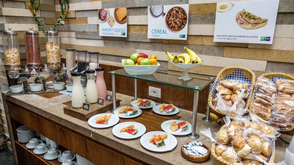 Mesa de buffet con frutas, panes, y cereales.