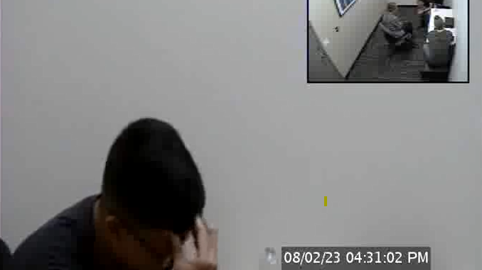 照片中，一名男子雙手抱頭，坐在審訊室的桌子旁。桌上放著一瓶水，照片模糊不清。右上角插入了一張較小的照片，從上方俯瞰審訊室，可以看到兩名聯邦調查局特工的全貌。