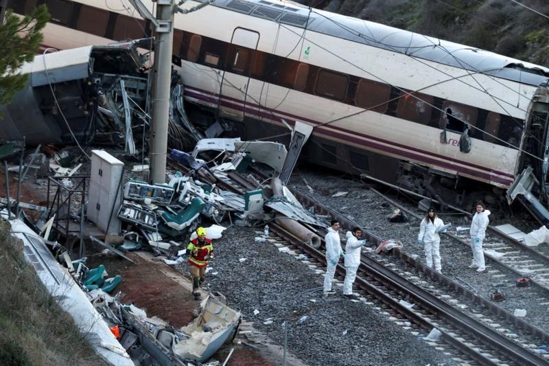 Vagones de tren yacen sobre la vía férrea tras el accidente en España, mientras investigadores examinan los escombros