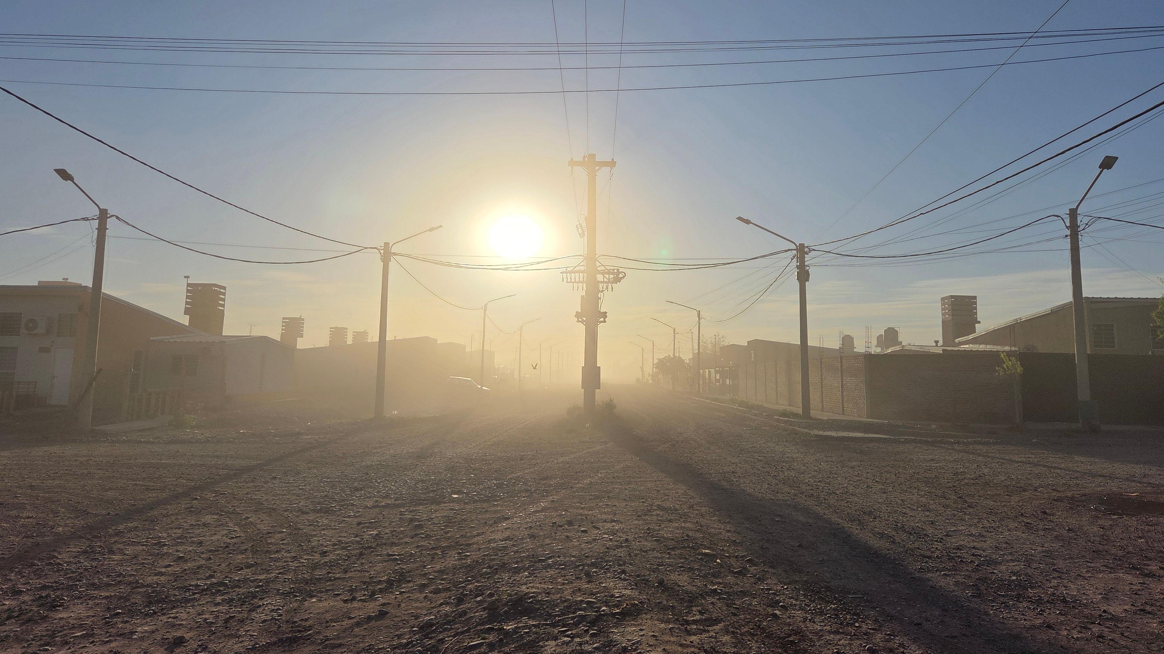 Rua de terra, nuvem de pó e o sol do amanhecer