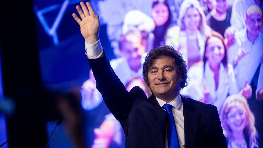 Javier Milei saluda a sus seguidores en un evento en la noche.