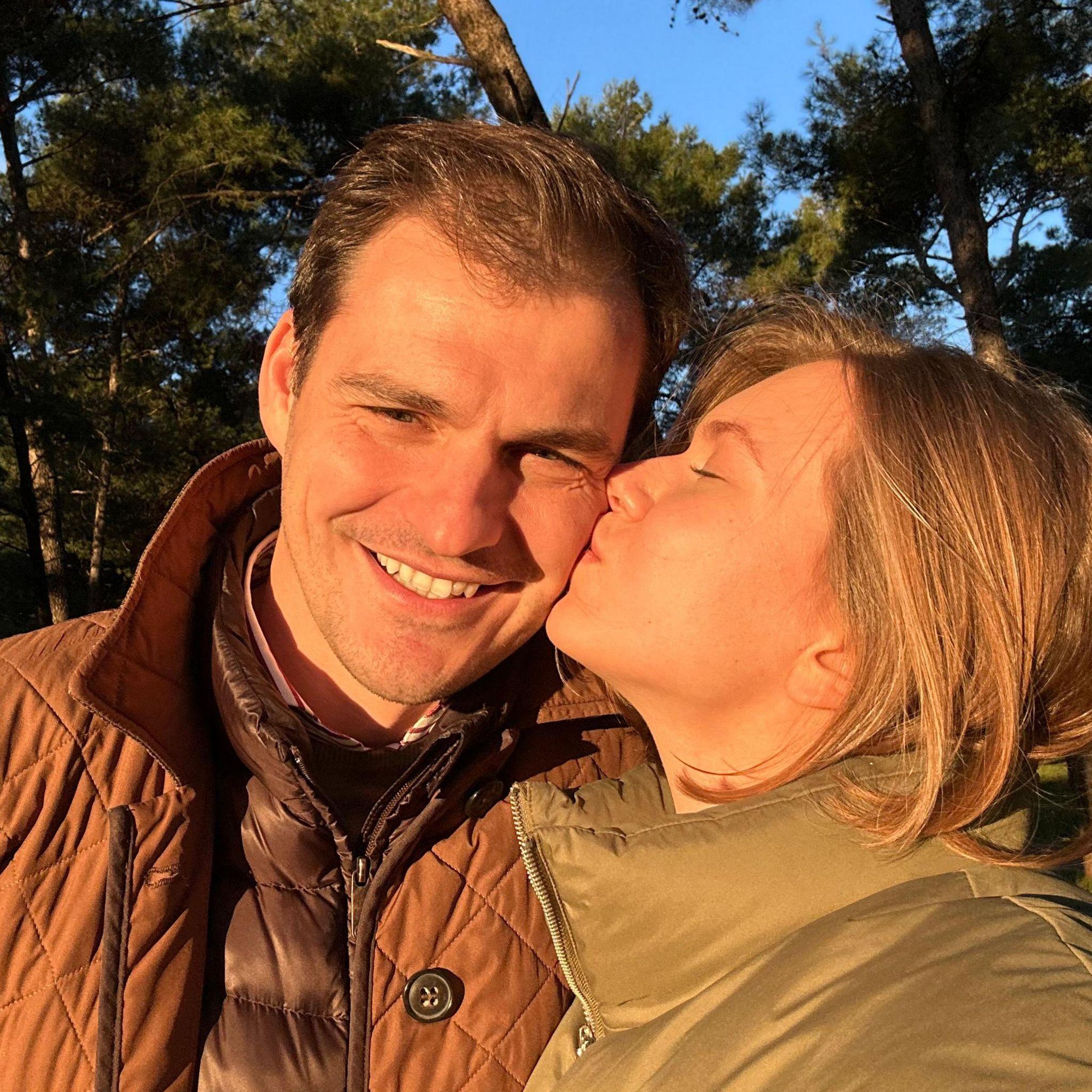 Kseniia le da un beso en la mejilla a Mikhail que sonríe y mira a la cámara mientras el sol se posa sobre el rostro de ambos.