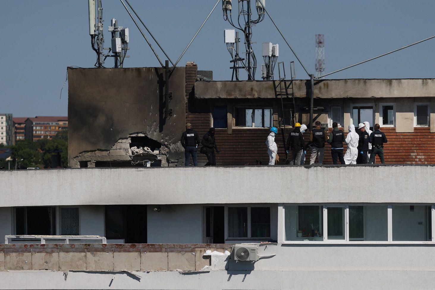11 funcionarios de Rumania, algunos vestidos de civil con chalecos negros y otros con trajes blancos y cascos inspeccionan la azotea del edificio. En la pared se ve un agujero