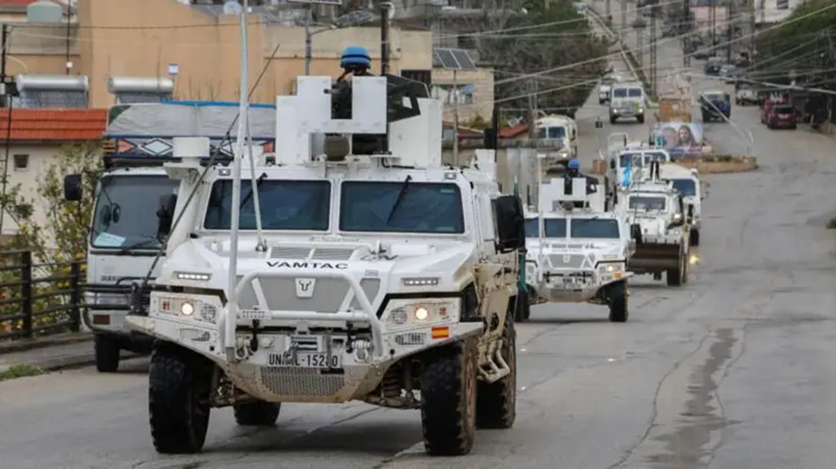 Kendaraan lapis baja dengan warna abu-abu terlihat berbaris di jalan dengan tentara di atasnya sedang berjaga.