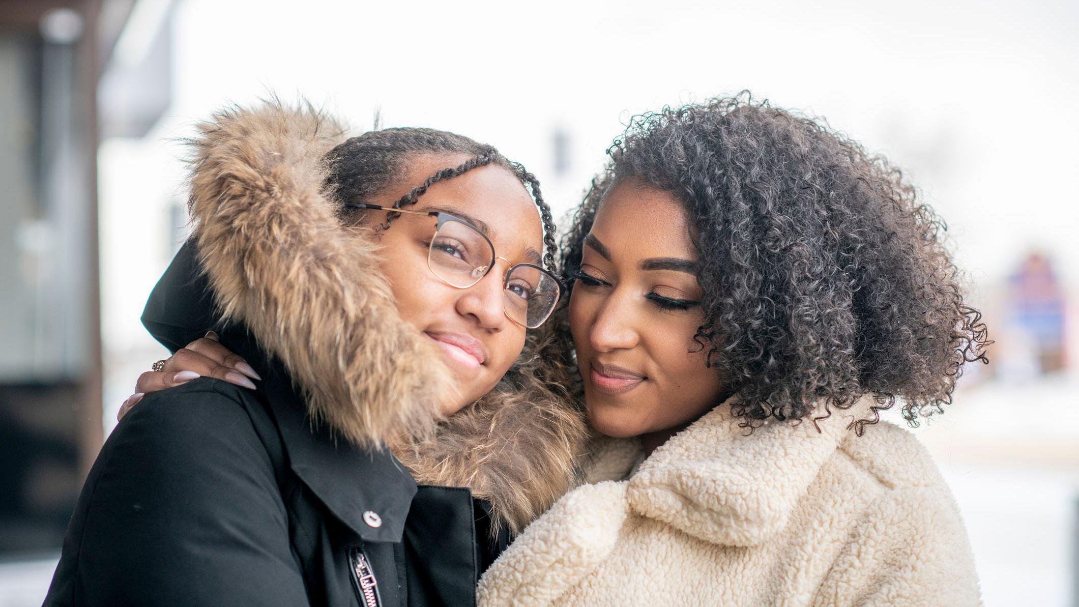 Mãe e filha ao ar livre na cidade durante o inverno, usando casacos para se manter aquecidas