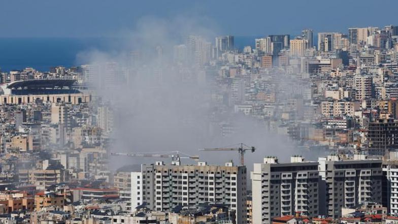 Una columna de humo se eleva en medio de una zona urbana con edificios y residencias en Beirut. El mar se ve en el fondo 