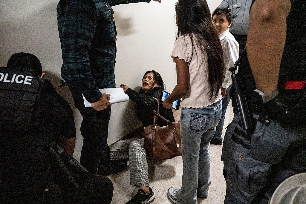 Mónica Moreta Galarza en el suelo, llorando, luego de ser atacada por un agente de ICE. Sus hijos están alrededor. 