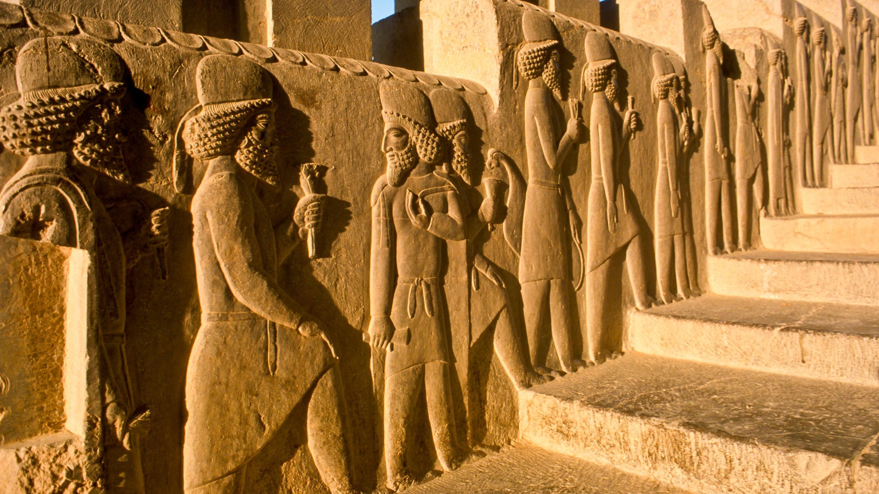 Baixo-relevo de figuras que adornam uma escada do palácio de Persépolis, mostrando uma fila que parece subir a escada sob a luz brilhante do sol