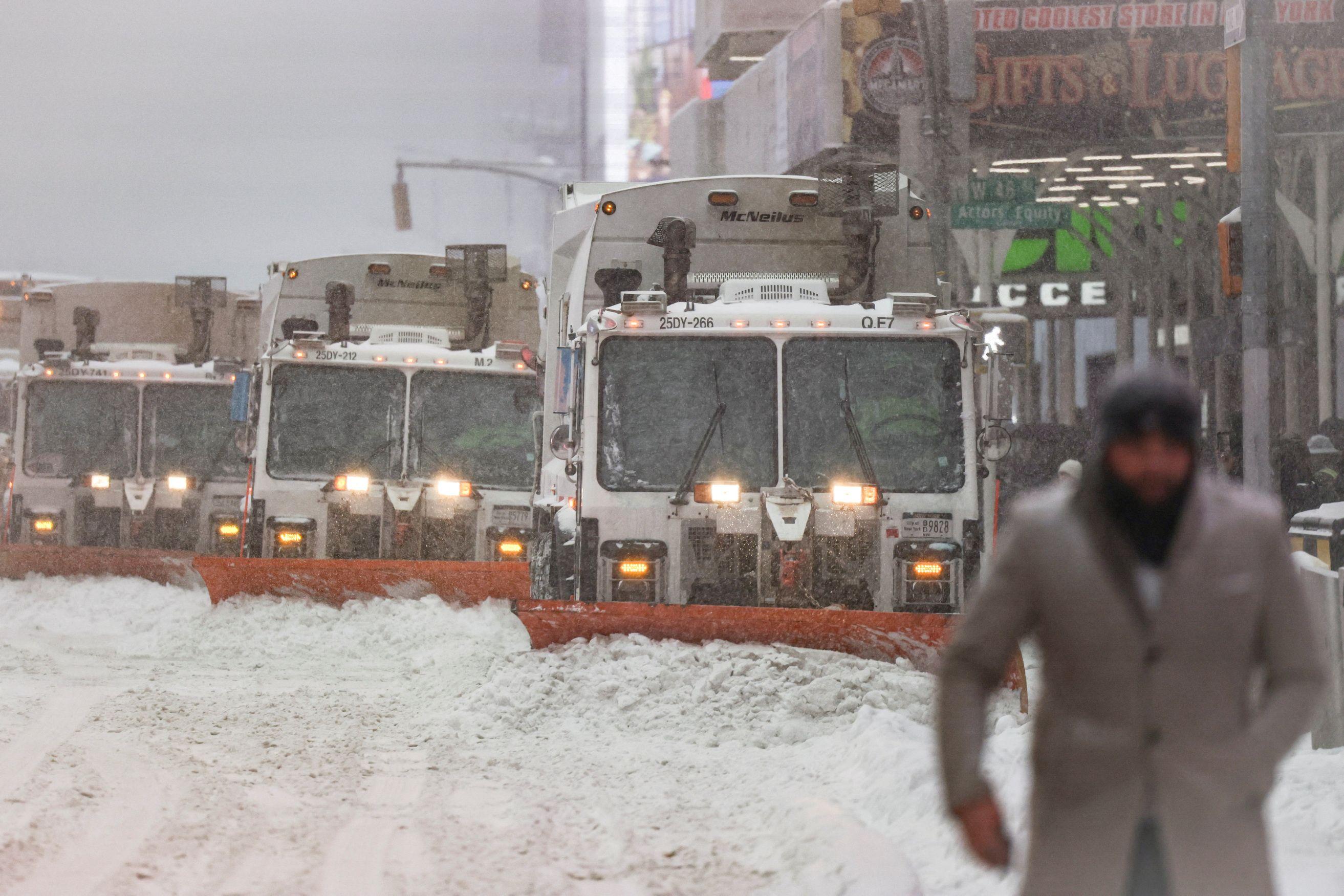 U prvom planu muškarac sa kapom i šalom u sivom kaputu, u drugom planu kamioni koji čiste sneg sa ulice 