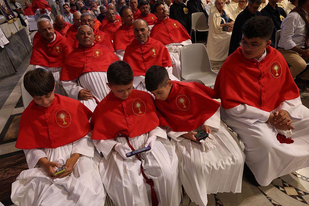 Membros de uma confraria cat&oacute;lica maltesa, incluindo crian&ccedil;as que est&atilde;o olhando para seus smartphones, participam do evento de boas-vindas na Bas&iacute;lica de S&atilde;o Jo&atilde;o de Latr&atilde;o durante o Jubileu das Confrarias em 16 de maio de 2025 em Roma, It&aacute;lia.