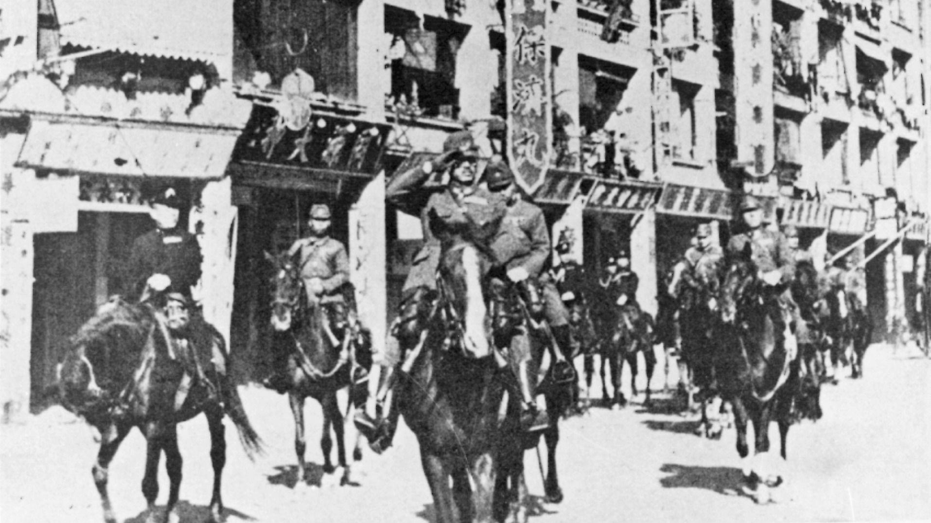 日軍佔領香港並舉行入城式，陸軍中將酒井隆（中）騎馬帶領隊伍行經灣仔軒尼詩道同源大押時，向路旁列隊的日軍士兵回禮（26/12/1941）