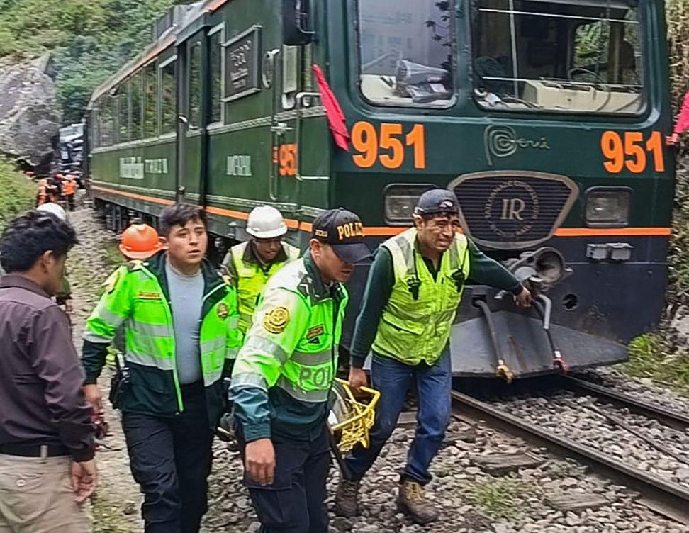Miembros de equipos de rescate con chalecos amarillos cargan una persona herida en una camilla al lado de un tren