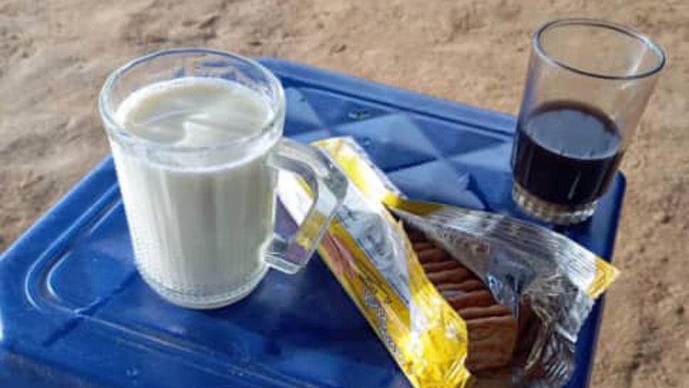 Banco de plástico azul com um copo de leite, um copo de café e um pacote de biscoitos.