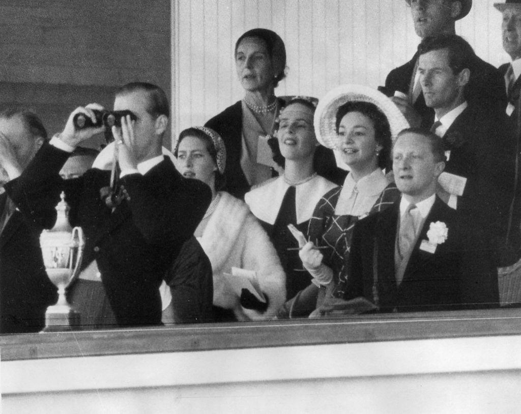 Un grupo de personas de alta sociedad observando una carrera de caballos desde un palco.