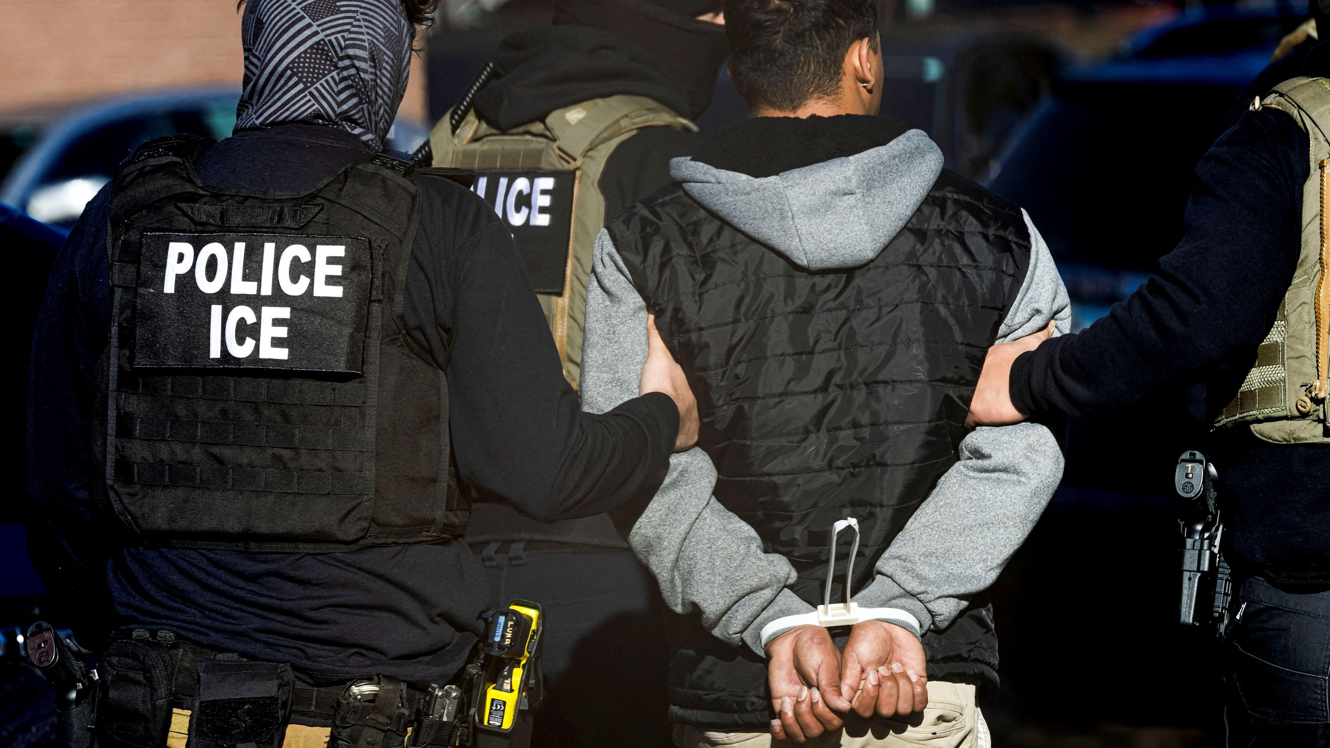 Agentes do ICE detendo um imigrante algemado, eles são vistos de costas