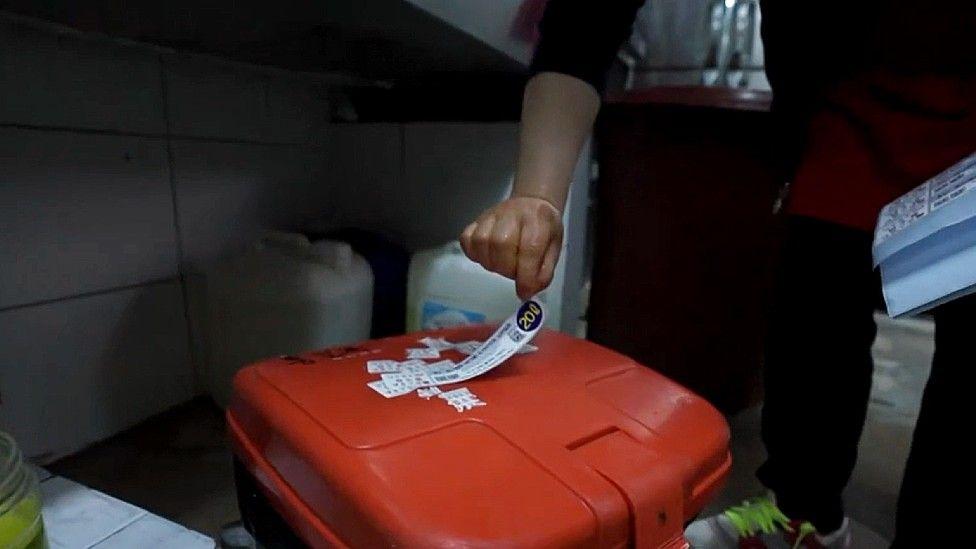 Mão de uma pessoa colando um adesivo em uma lata de lixo vermelha