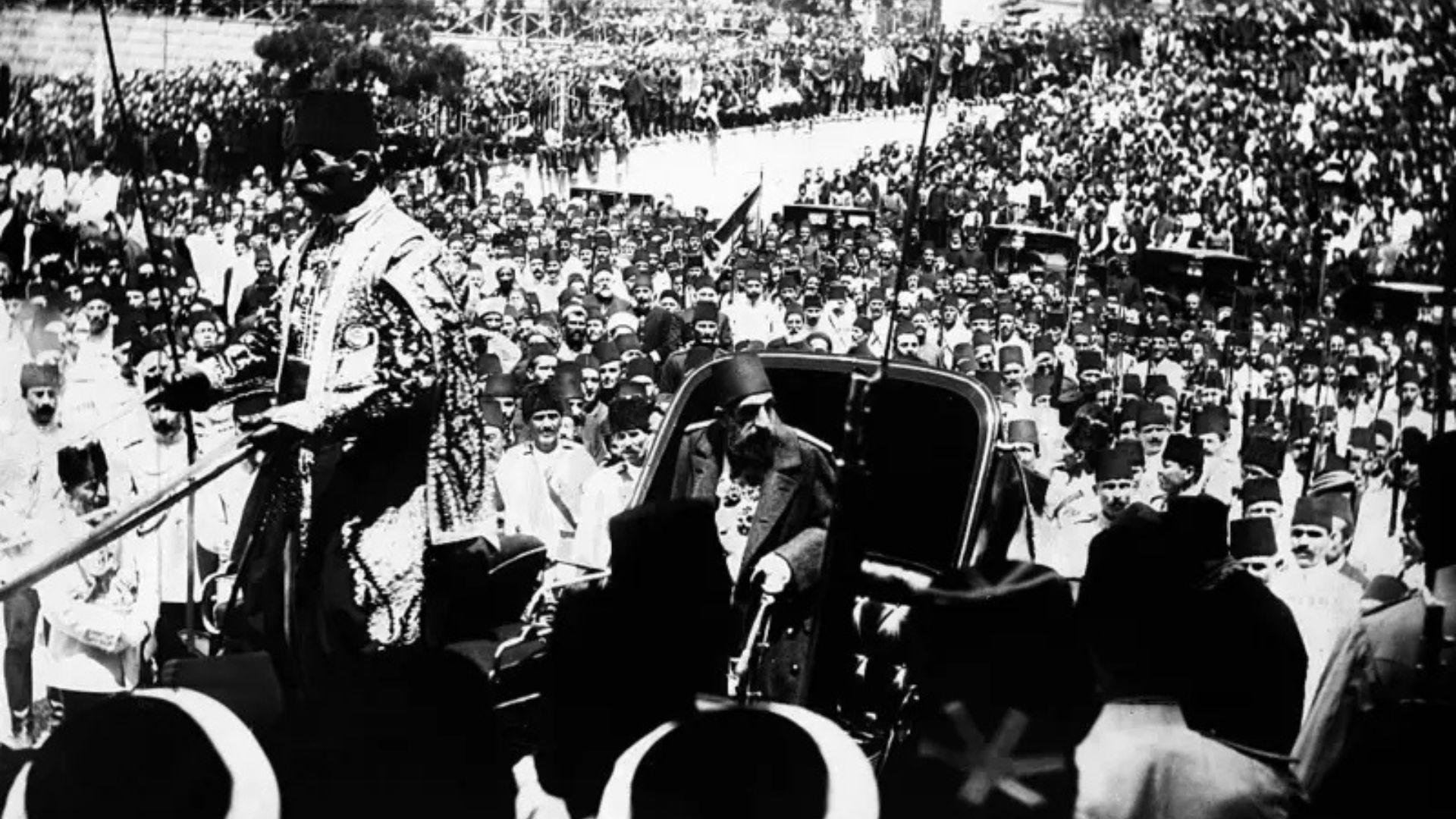 Uma fotografia em preto e branco de Abdul Hamid 2º, de 1908, andando numa carruagem puxada por cavalos e rodeado por uma multidão