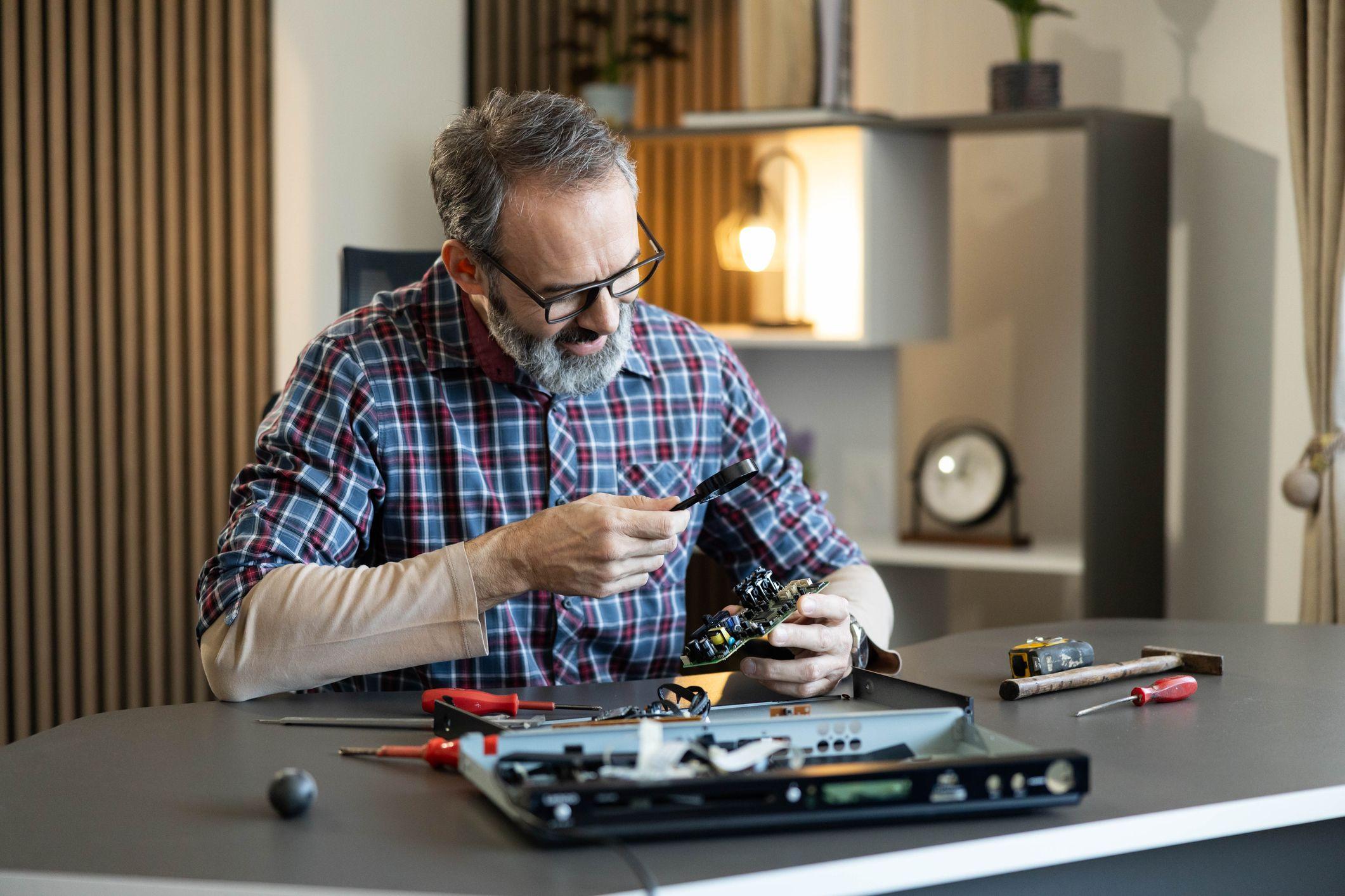 Un hombre reparando una tarjeta de memoria de un computador. Sostiene una lupa en su mano.
