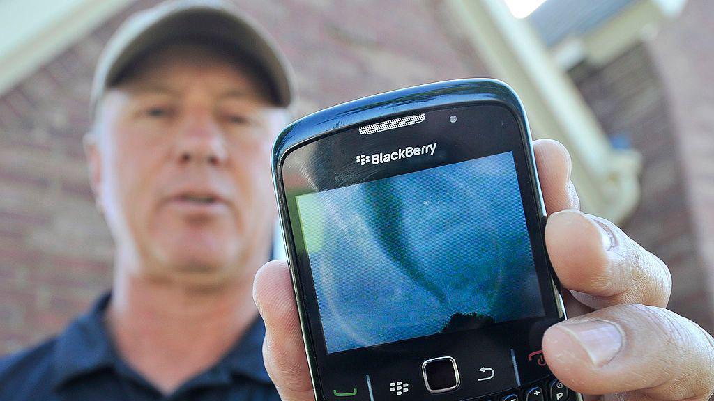 Um homem de bon&eacute; mostra o registro de um tornado na tela de seu celular da marca BlackBerry, em Denton, Texas, em 2011