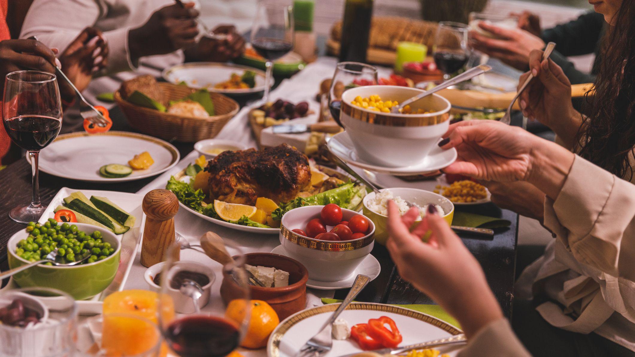 Mesa repleta de alimentos diversos com pessoas fazendo sua refei&ccedil;&atilde;o