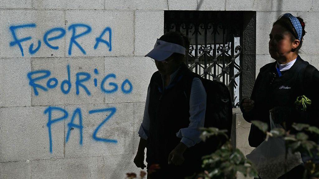 Mujeres pasan junto a un grafiti que dice "Rodrigo Paz fuera", en referencia al presidente de Bolivia, en La Paz, el 19 de mayo de 2026. 