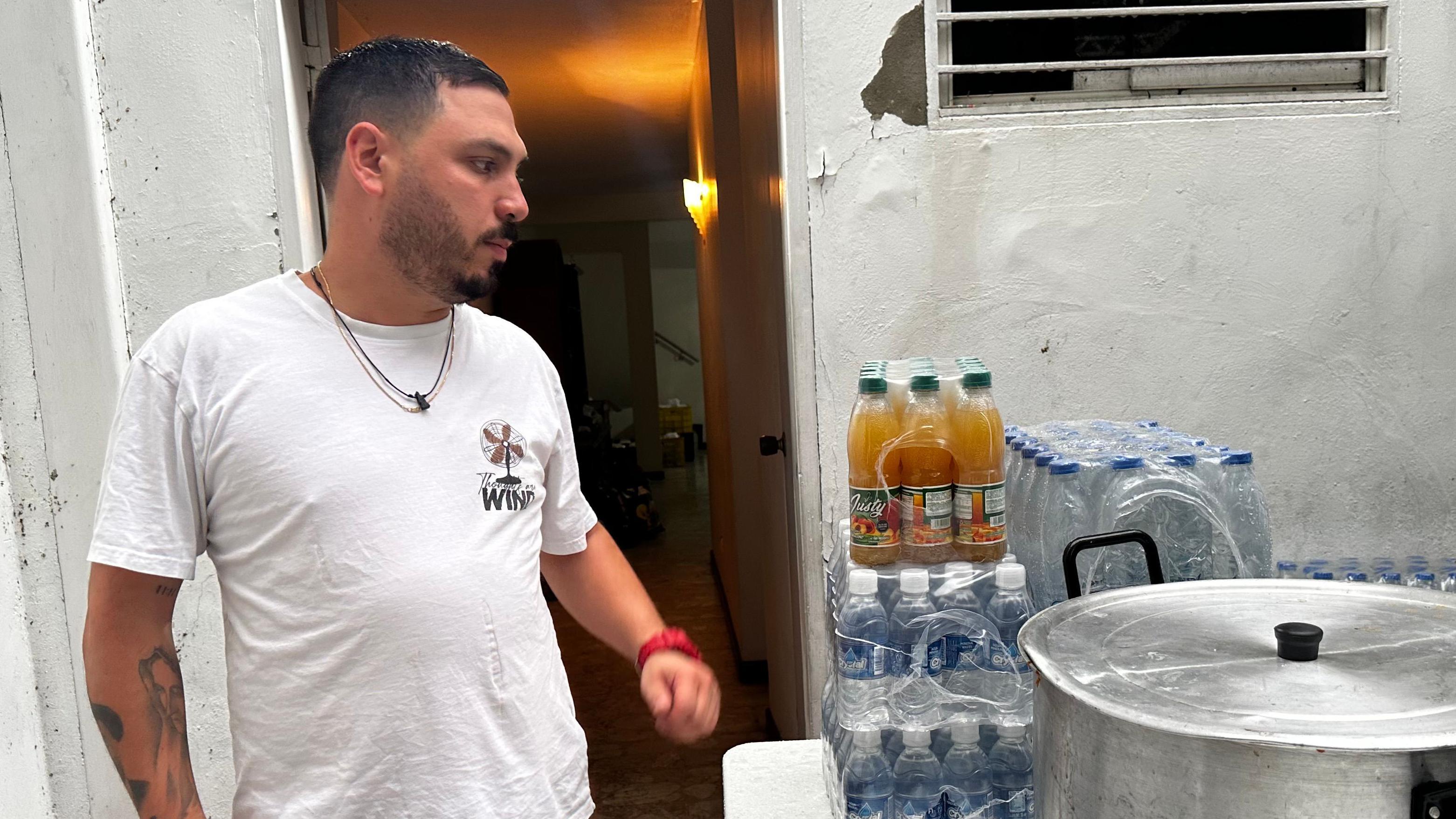 Víctor Andrea D'Orsi en el patio al lado de una olla y botellas de agua. Lleva una franela blanca.