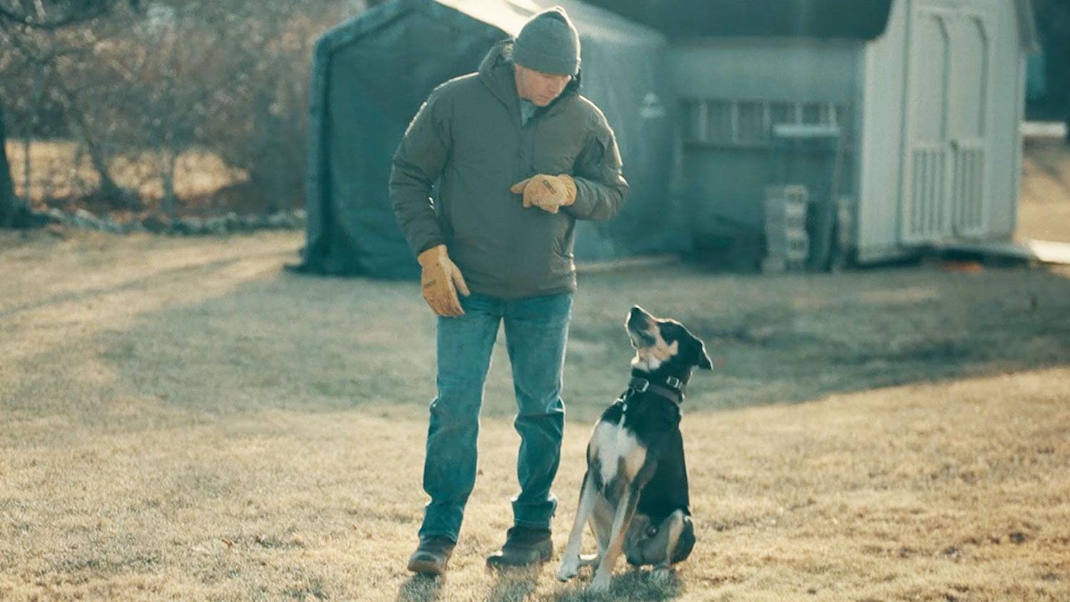 muškarac sa psom u šetnji blizu kuće - gleda odozgo u crno-belog i žutosmeđeg psa koji ga gleda
