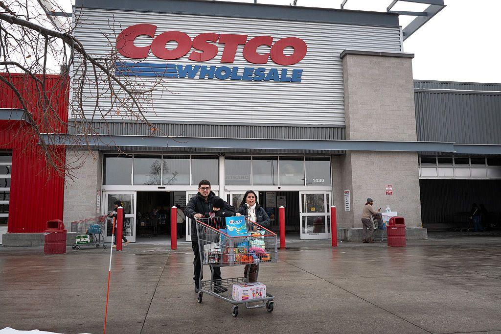 Una pareja empuja un carrito de supermercado a las afueras de un edificio con un gran letrero con letras rojas que dice Costco.