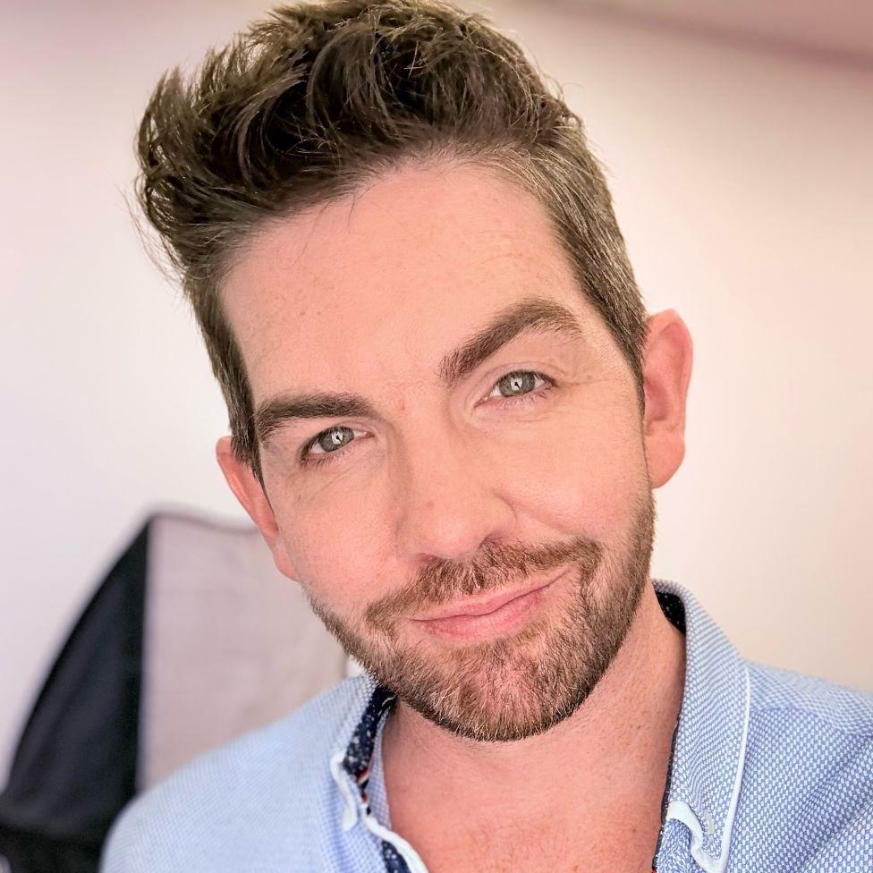 一位留著棕色短髮、身穿藍色襯衫的男子對著鏡頭微笑