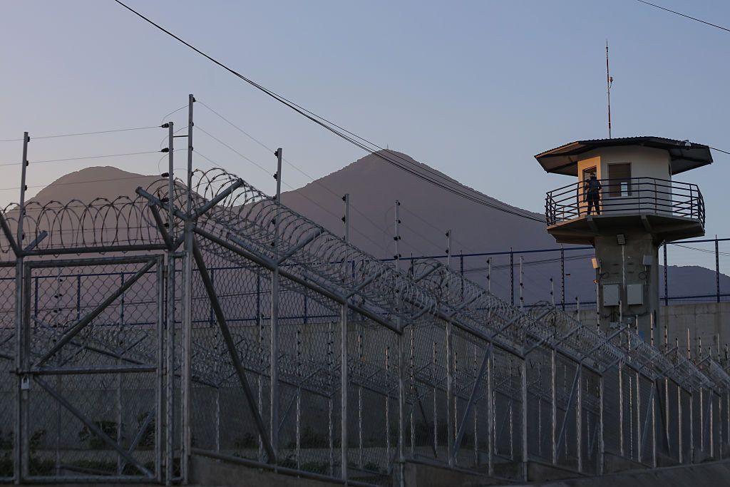 Un funcionario de prisiones hace guardia en la torre de vigilancia con el volcán San Vicente al fondo en el centro penitenciario de máxima seguridad CECOT (Centro de Internamiento Obligatorio para Terroristas) el 4 de abril de 2025 en Tecoluca, San Vicente, El Salvador.