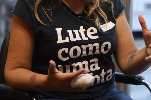 Michelle Bernardes fotografada do pesco&ccedil;o para baixo, com o dedo enfaixado ap&oacute;s incidente que resultou na amputa&ccedil;&atilde;o parcial do membro. Ela veste uma camiseta preta onde se l&ecirc; em letras brancas 