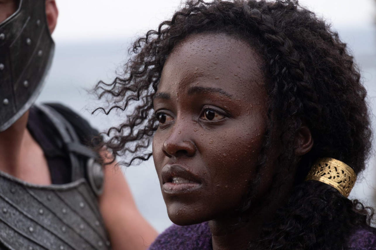 Lupita Nyong'o mira hacia la izquierda del encuadre con expresión preocupada, en un primer plano de su cabeza y hombros, mientras interpreta a Helena de Troya en "La Odisea" de Christopher Nolan.