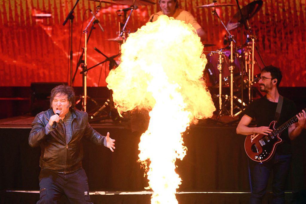 Milei canta con su banda de rock en un escenario con fuegos artificiales.