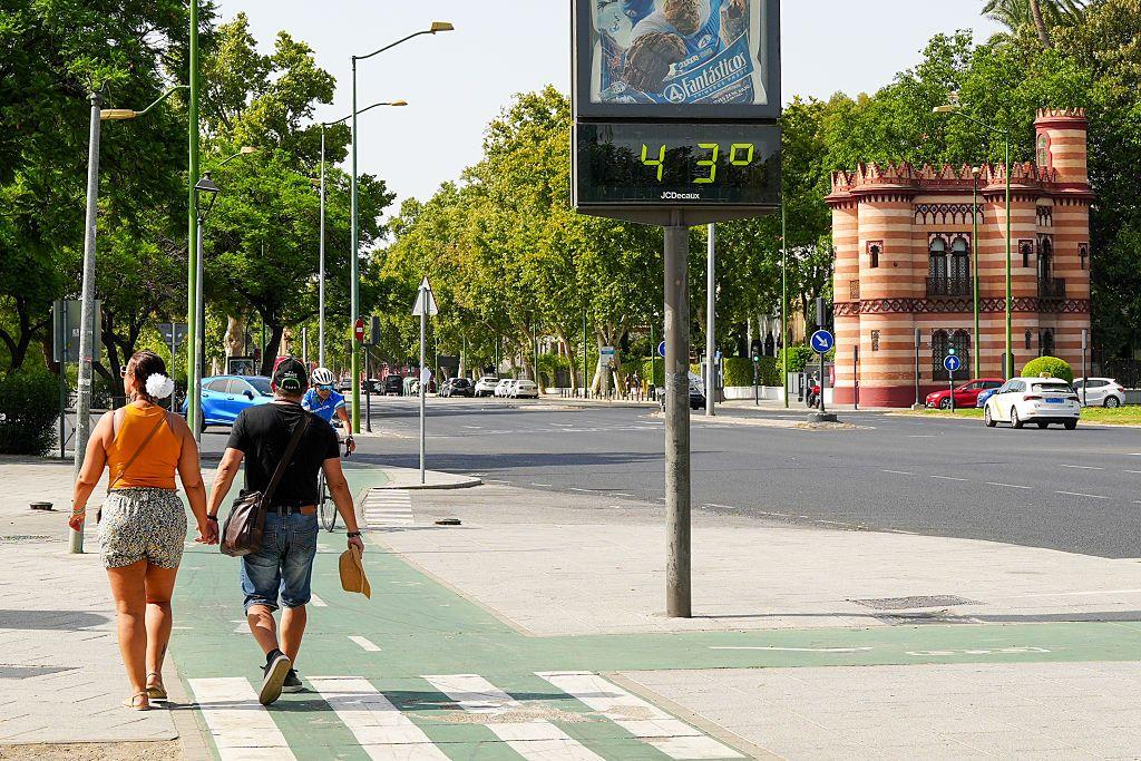 Pessoas andando na rua. Há um monitor de temperatura que registra 43 graus Celsius. 