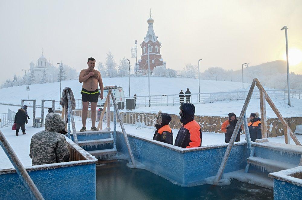 Čovek se priprema da skoči u ledenu vodu dok spasioci stoje u blizini tokom proslave pravoslavnog hrišćanskog praznika Bogojavljanja u sibirskom gradu Krasnojarsku, Rusija, u januaru 2026.