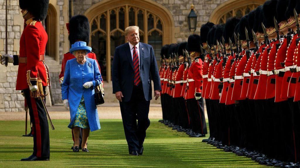 Donald Trump camina junto a la reina Isabel II de Inglaterra, mientras ambos pasan revista a la Guardia Real británica formada con su tradicional uniforme rojo y negro en el castillo de Windsor. 