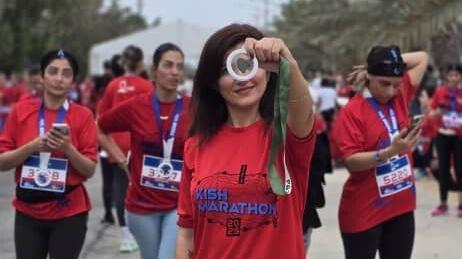 Mulheres iranianas vestem uma camisa vermelha com a logo da maratona. Uma delas mostra uma medalha 