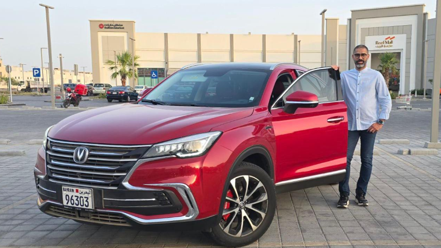 الحيقي مرتدياً قميصا أزرق وبنطالاً من الجينز، يقف إلى جوار سيارة حمراء اللون لامعة