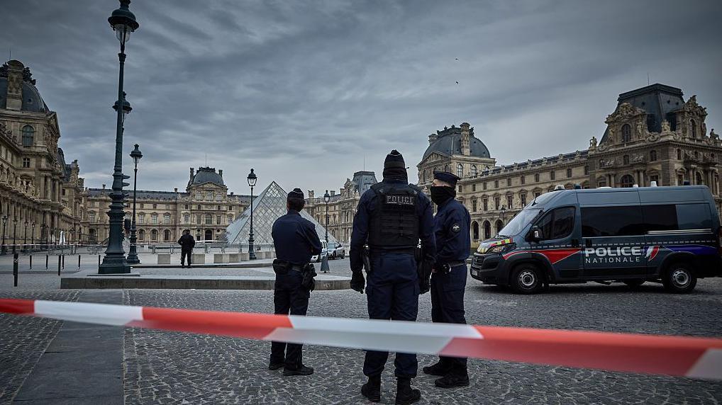 La policía francesa sella el perimetro del museo con cintas blancas y rojas. A lo lejos se ve vehiculos policiales. 