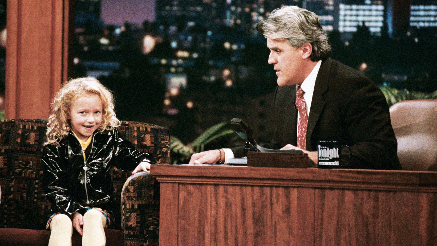 La actriz Hayden Panettiere, que tiene el pelo rubio rizado y lleva una chaqueta negra brillante, durante una entrevista con el presentador Jay Leno el 3 de octubre de 1996. 