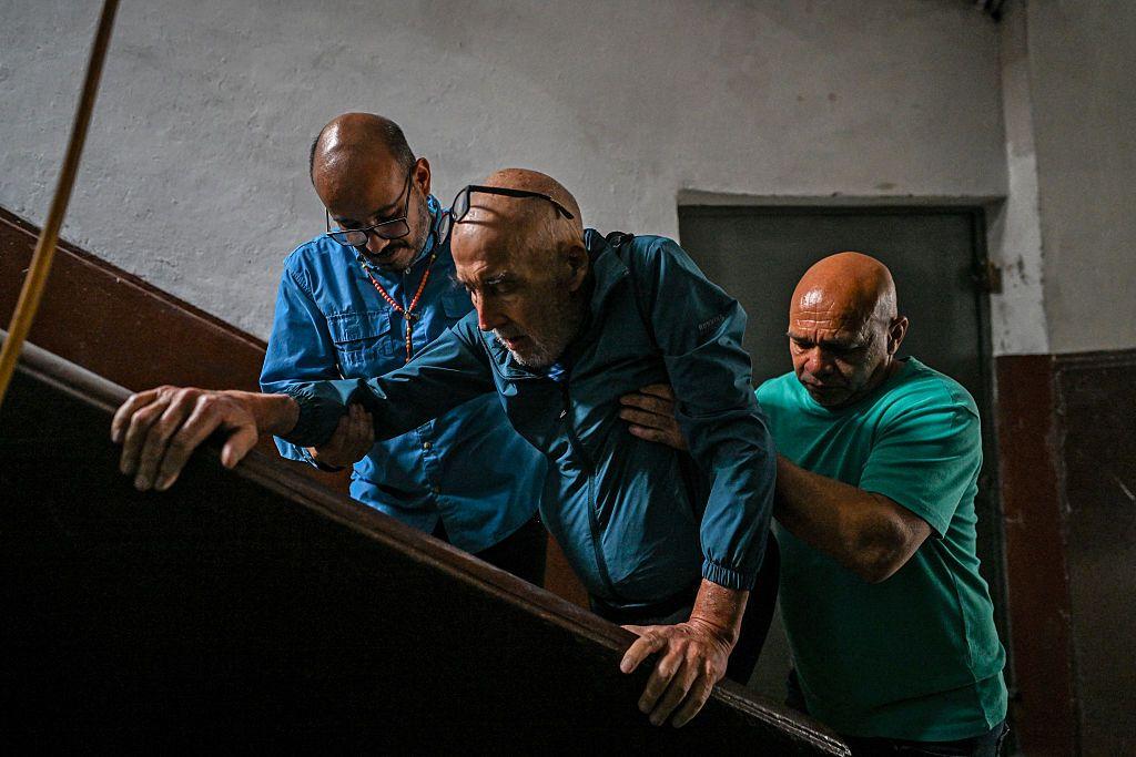 Dos hombres ayudan a Breijo, de 71 años, a subir las escaleras