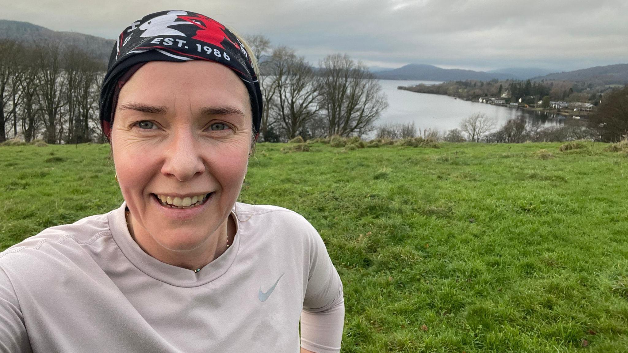 Uma mulher com um lenço estampado cobrindo o cabelo tira uma selfie em frente a um campo gramado e um lago