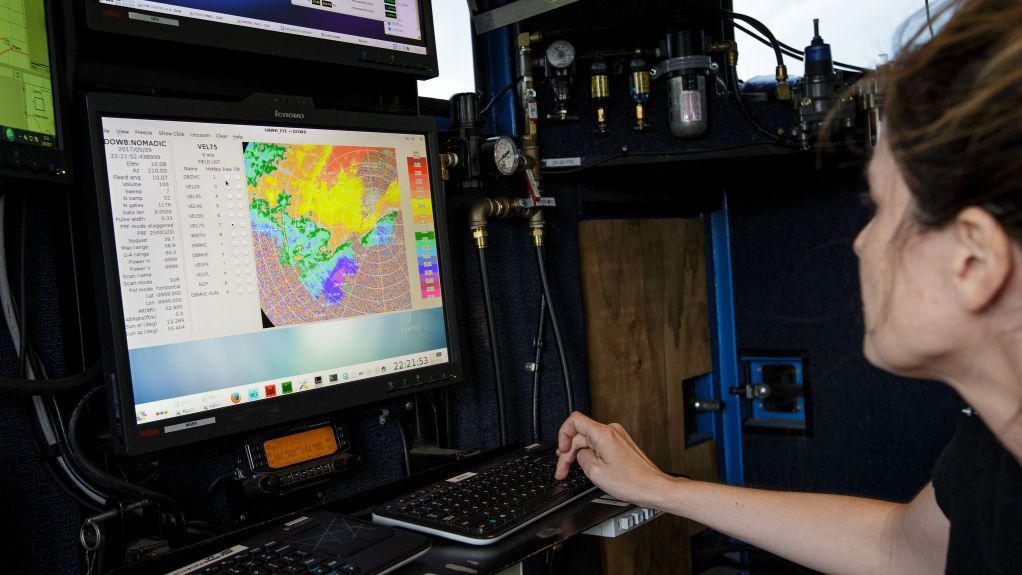 Uma meteorologista monitora uma tempestade a bordo do ve&iacute;culo Doppler on Wheels. Ela veste camiseta preta e observa uma tela de computador com uma imagem colorida