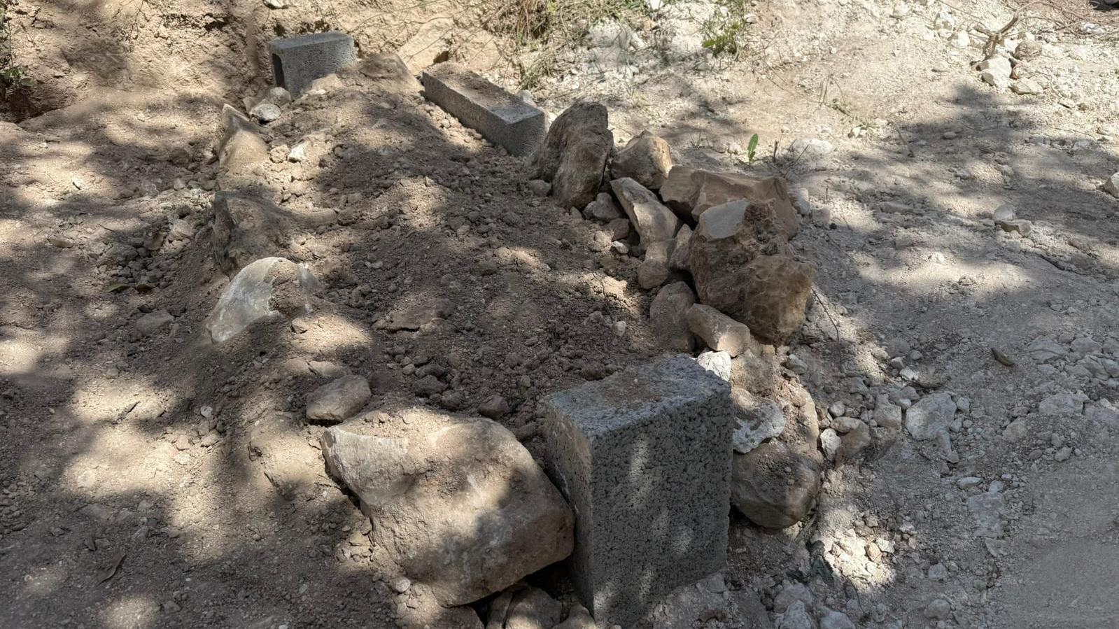 Una tumba recién cavada con tierra en el centro rodeada de rocas de distintos tamaños