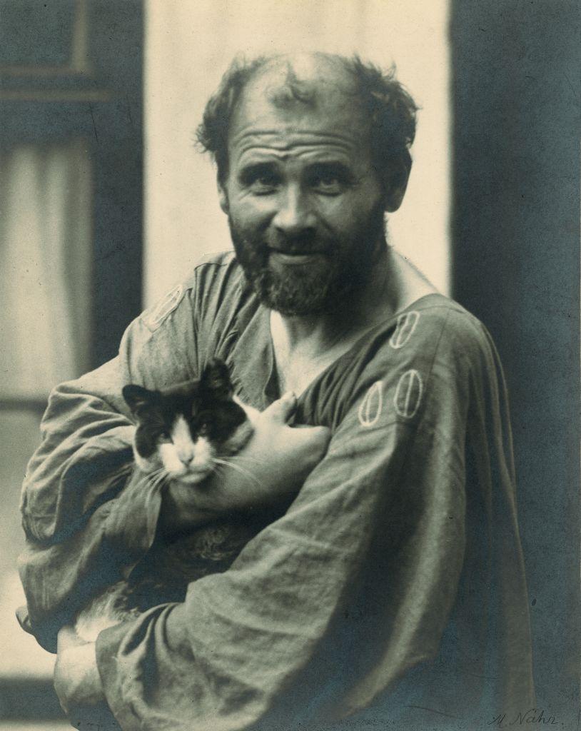 Gustav Klimt mira a la cámara mientras carga un gato en sus brazos