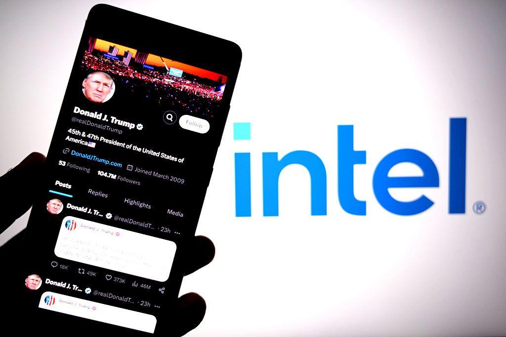 Una mano sostiene un teléfono móvil cuya pantalla está abierta en la cuenta de Donald Trump en redes sociales. En el fondo está el logo de Intel en letras azules