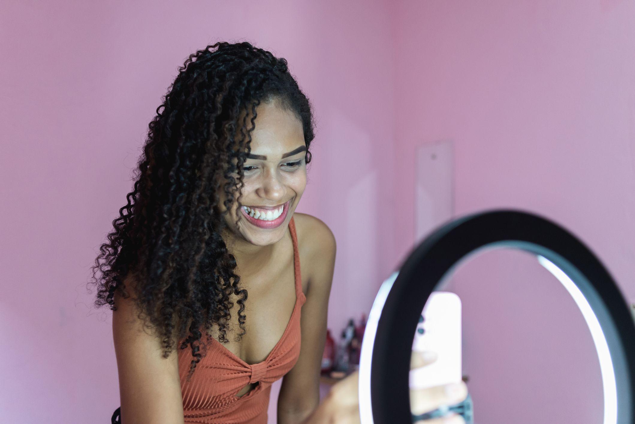 Una mujer joven sonriente se prepara para hacer una grabación de video con un iPhone y una luz circular.