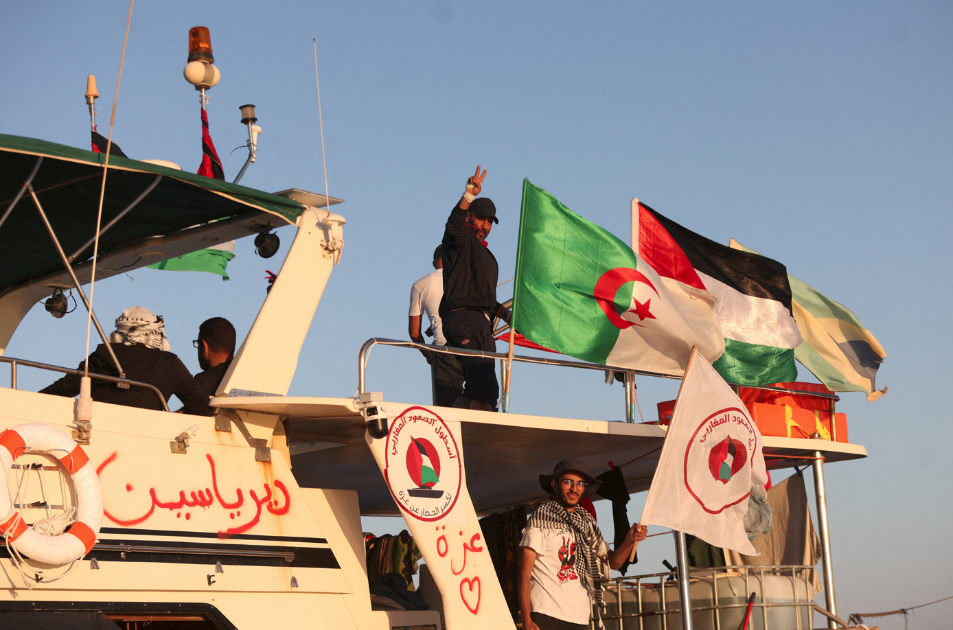 Miembros de la Global Sumud Flotilla saludan abordo de un barco junto a varias banderas