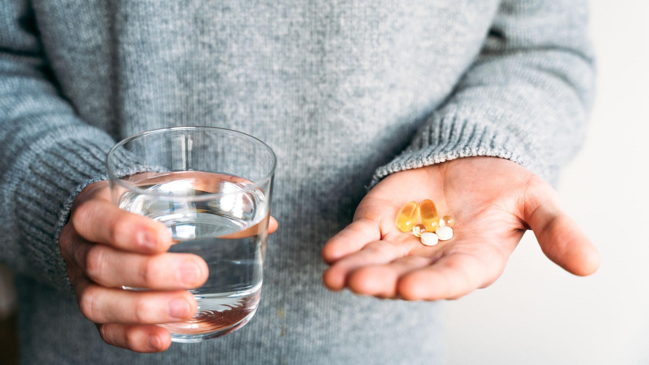 una persona tiene en una mano varias pastillas y en la otra un vaso con agua